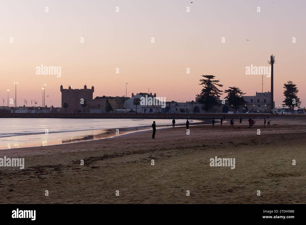 Le persone giocano sulla spiaggia al tramonto con la medina alle spalle nella città di Essaouira, in Marocco. 18 dicembre 2023 Foto Stock