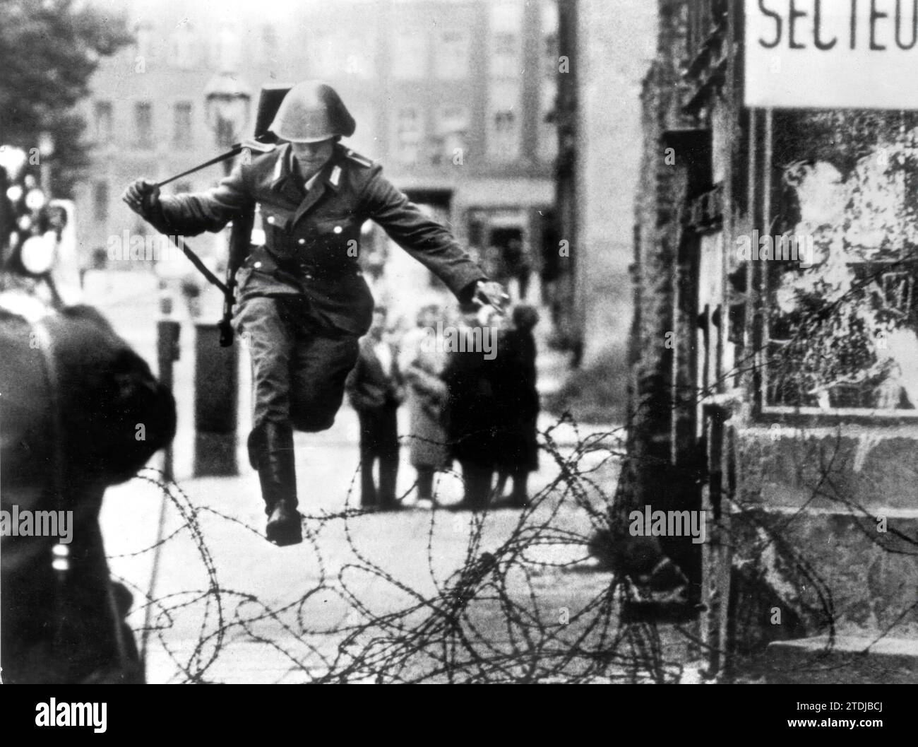 Il 13 agosto 1961, la RDT iniziò ad erigere recinzioni in filo spinato e un muro attraverso Berlino. Due giorni dopo, un agente della polizia popolare saltò, con tutta la sua attrezzatura, sugli ostacoli del filo spinato, verso il settore occidentale di Berlino. Crediti: Album / Archivo ABC Foto Stock