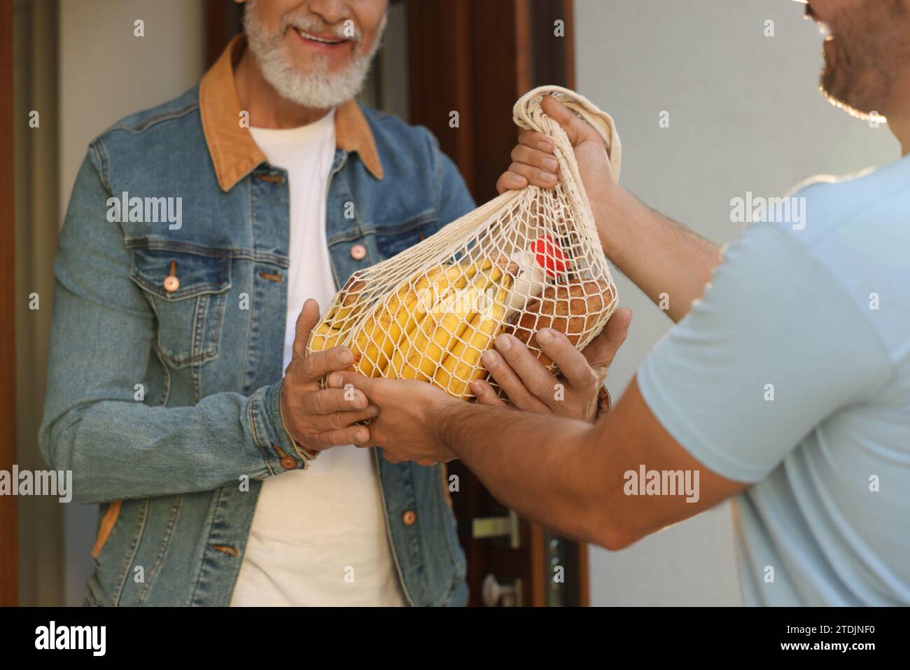 Uomo con un sacco di prodotti che aiuta il suo vicino più anziano all'aperto, primo piano Foto Stock