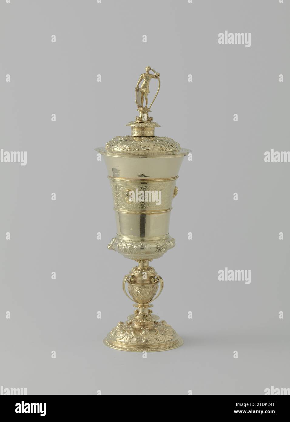 Calice con coperchio, Adriaen de Groet, 1561 - 1562 tazza con coperchio in argento dorato. Cartigli guidati e limiti di frutta sul piede sagomato e curvo, sul fondo allargato e sul coperchio a volta; su quest'ultimo anche i mascaron. Il nodus a forma di vaso, decorato, è contenuto in quattro morsetti forati a forma di nastro. Il calice dilatante è diviso in tre strisce orizzontali da due profili; solo quello centrale è decorato: Tre teste rialzate (gioventù, età adulta e vecchiaia) su uno sfondo di raffinato lavoro di banda e Maurkenken. Il coperchio è coronato da un guerriero schermato su un pied-de-stable doppio. t Foto Stock