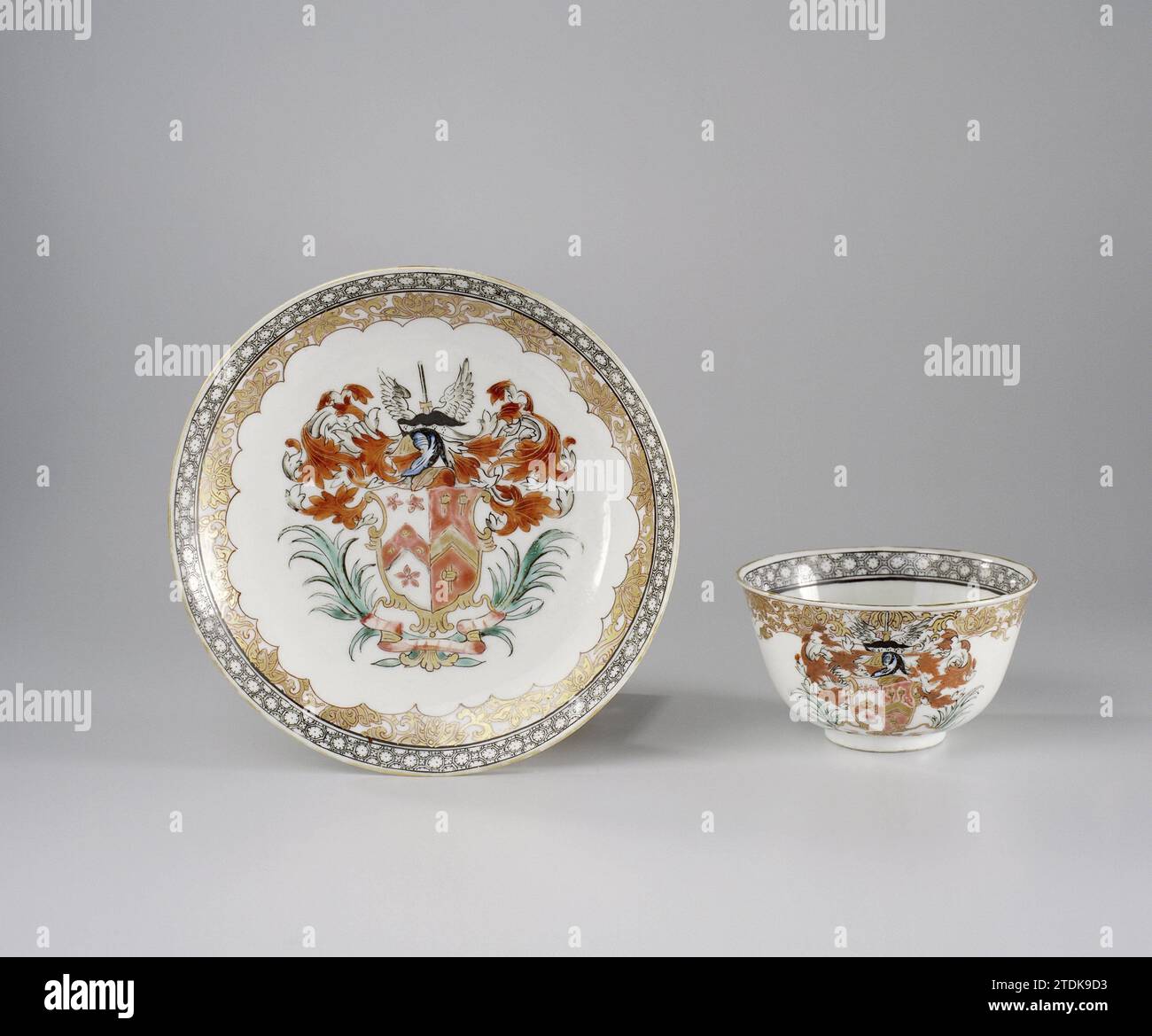 Tazza a forma di campana e piattino con le braccia della famiglia Yaldwin e Soame, anonimo, c. 1740 - c. 1760 testa a forma di campana e piatto di porcellana, dipinti sullo smalto in blu, rosso, rosa, verde, nero e oro. Sul piatto l'arma delle famiglie Yaldwin e Soame. A sinistra Yaldwin con tre fiori su sfondo bianco e al centro un twill rosso con due bulbi gialli e una testa di leone; a destra socen con tre martelli su sfondo rosso e un twill dorato al centro. Il segno del casco è una spada alata circondata da foglie di acanto. Un ramo di palma su entrambi i lati della piaga Foto Stock