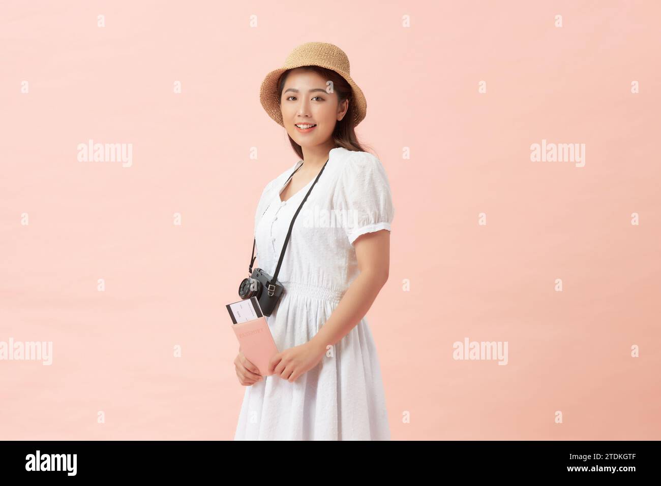 Una donna turistica felice che indossa un cappello con i biglietti per la fotocamera sembra isolata su sfondo rosa Foto Stock