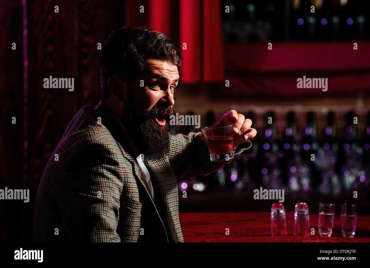 Uomo lavoratore vintage con barba lunga che tiene il whiskey. Seduto al bar. Foto Stock