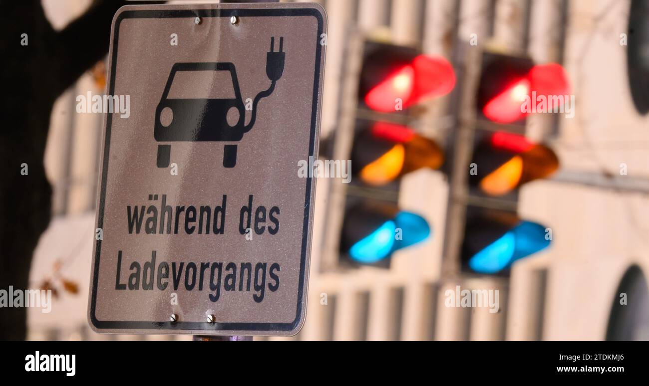 19 dicembre 2023, bassa Sassonia, Hannover: Un cartello con il simbolo di un'auto elettrica e le parole "in carica" indicano un parcheggio presso una stazione di ricarica. I tre colori di un semaforo si illuminano sullo sfondo (esposizione lunga). Dopo la fine improvvisa del premio di acquisto per le auto elettriche, i clienti sono ora esclusi dal freddo. L'industria protesta e si lamenta di una perdita di fiducia nella politica. Nell'ambito del loro programma di austerità, alcuni giorni fa i leader della coalizione SPD, Verdi e FDP hanno concordato di eliminare gradualmente le sovvenzioni statali "prontamente”. Foto: Julian Stratenschulte/d Foto Stock