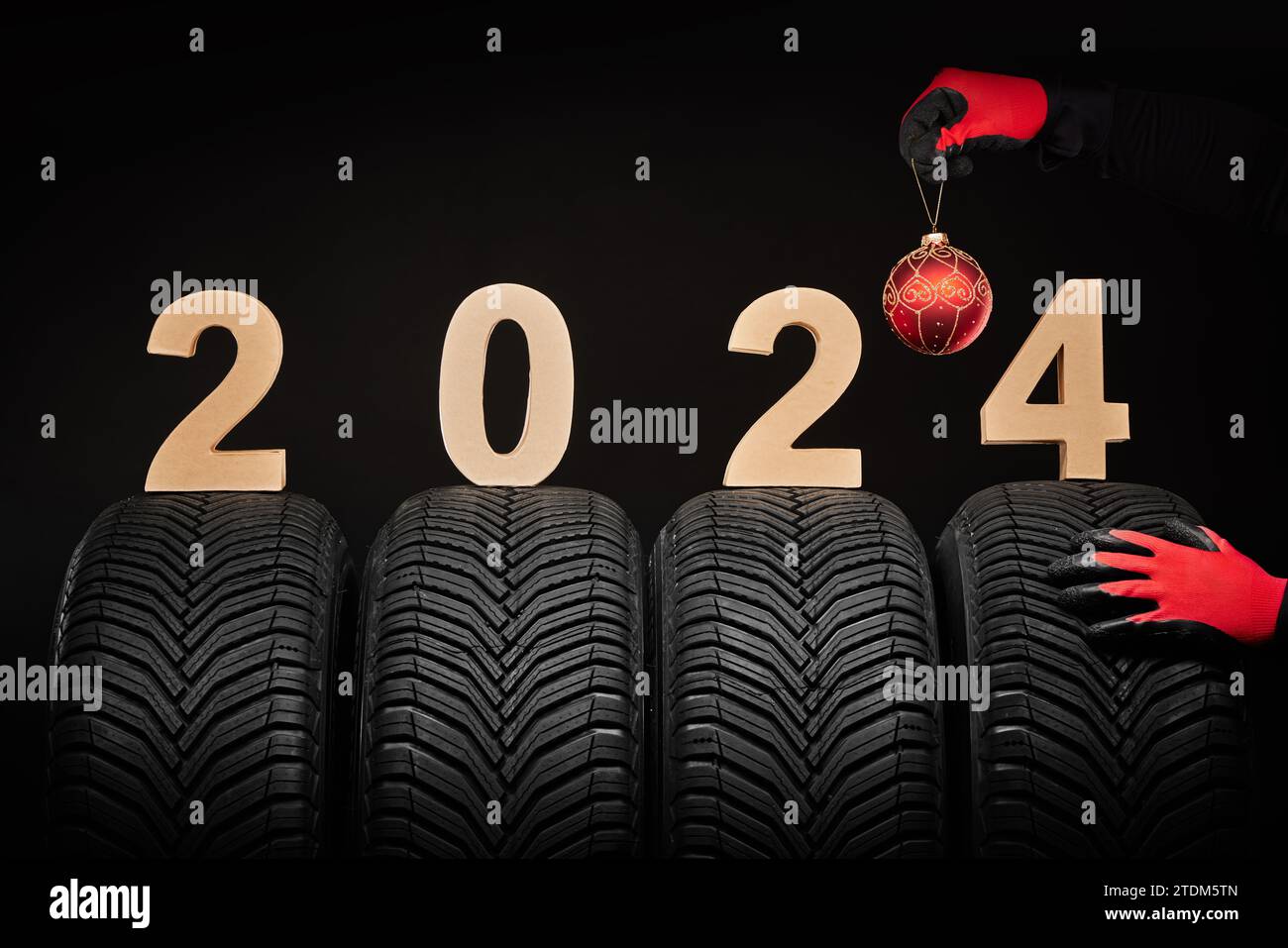 2024 felice anno nuovo, gomme invernali e mani di un uomo con palla d'albero di natale su sfondo nero Foto Stock