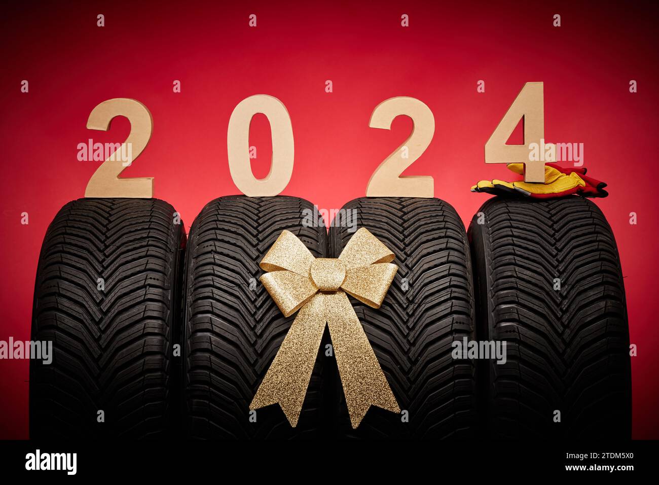 Pneumatici auto, pneumatici nuovi, ruote invernali nastro di fiocco dorato presente, testo 2024 buon anno natale sfondo. Foto Stock