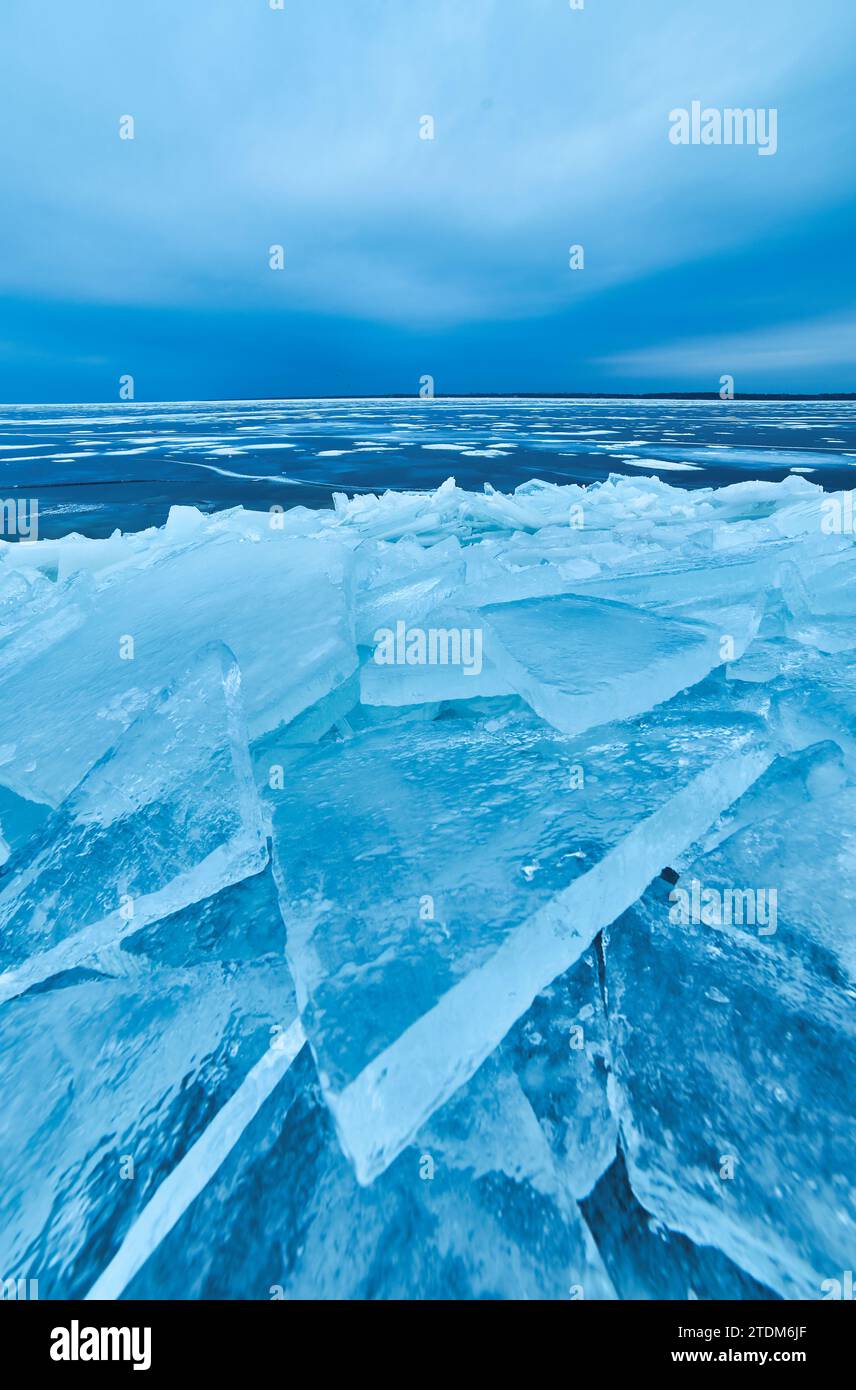 Una suggestiva vista invernale con una calotta di ghiaccio blu cristallina che avvolge delicatamente la riva del lago in un'incredibile esposizione di bellezza naturale ghiacciata Foto Stock