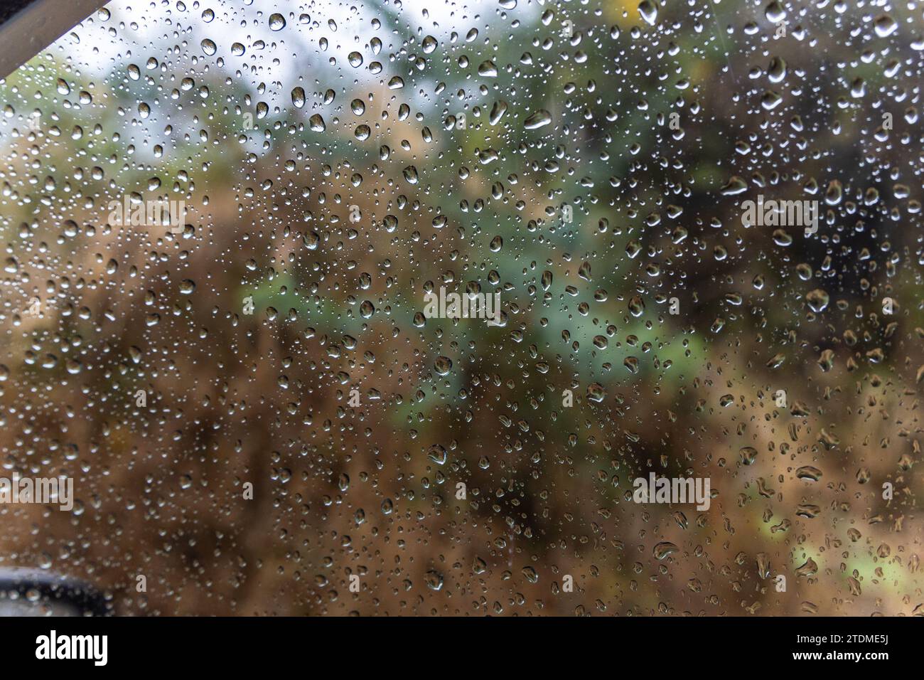 gocce di pioggia che scivolano sul vetro del finestrino dell'auto durante le giornate piovose da un angolo piatto Foto Stock