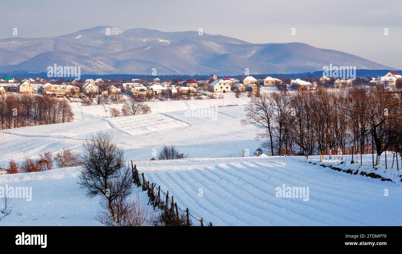 paesaggio di campagna montuoso la sera d'inverno. scenario con campi rurali innevati. villaggio transcarpaziano in lontananza Foto Stock