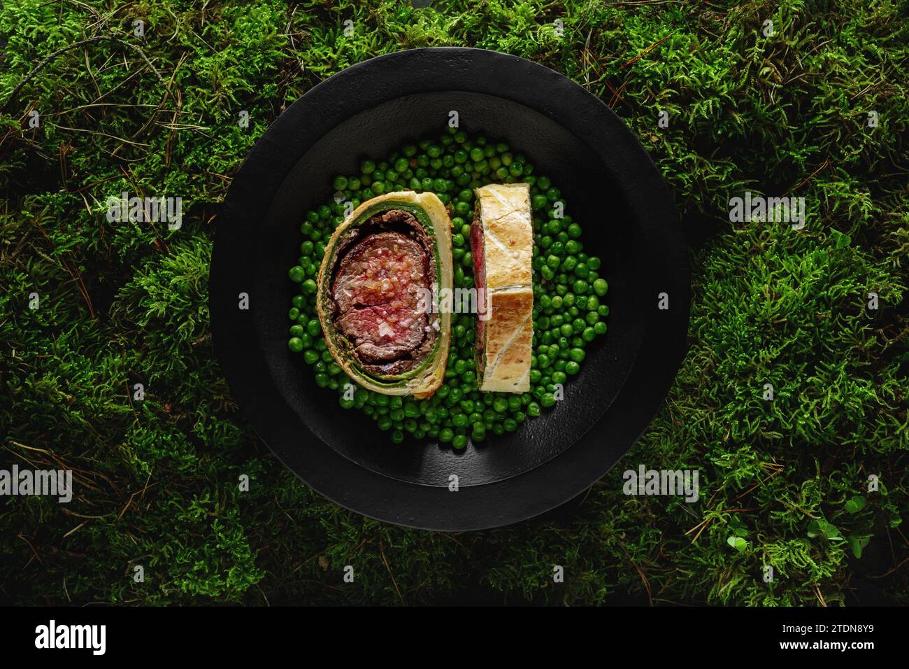 Manzo natalizio fatto in casa Wellington come creazione dell'avvento servito in piatto nero con pipi verdi su sfondo muschio di forrest. Placcatura alimentare ed estetica co Foto Stock