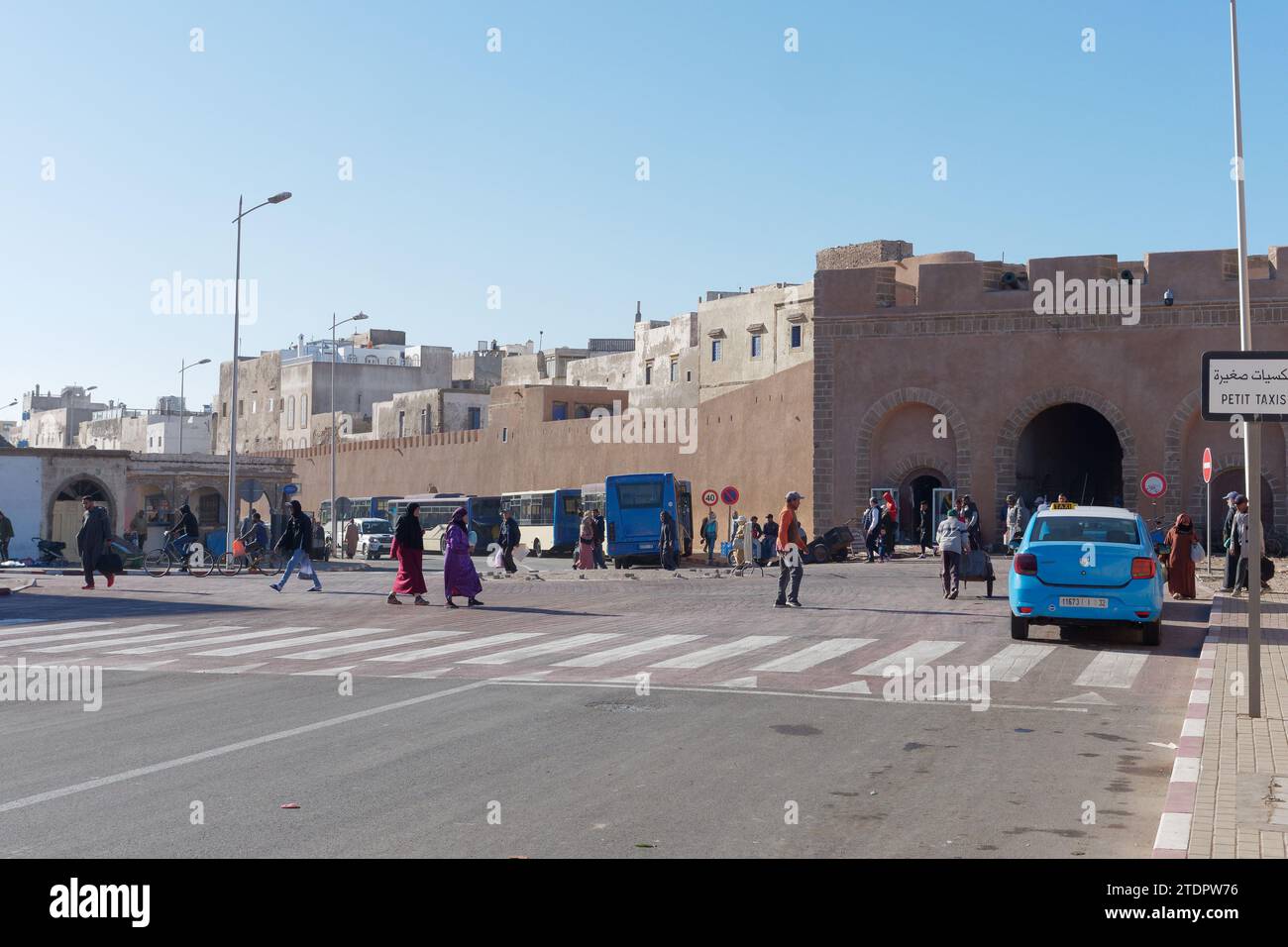 Taxi blu e autobus attendono su una strada con passaggio pedonale fuori dalle mura della medina nella città di Essaouira, in Marocco. 19 dicembre 2023 Foto Stock