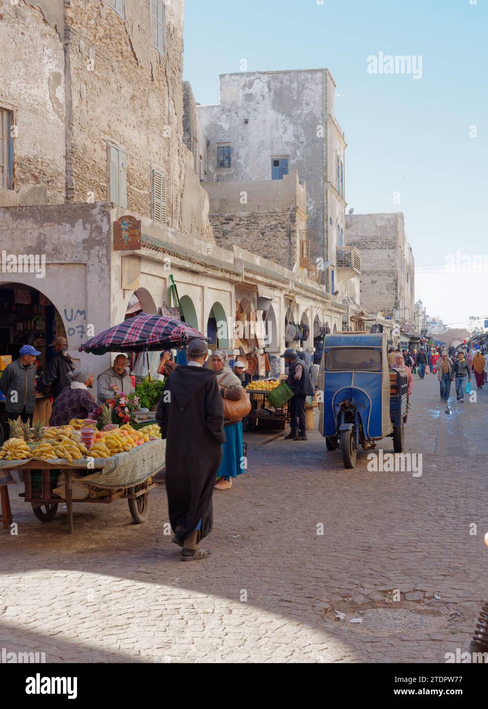 Strada trafficata con venditori ambulanti e motociclette con copertura e bancarelle di frutta nella medina della città di Essaouira, Marocco. 19 dicembre 2023 Foto Stock