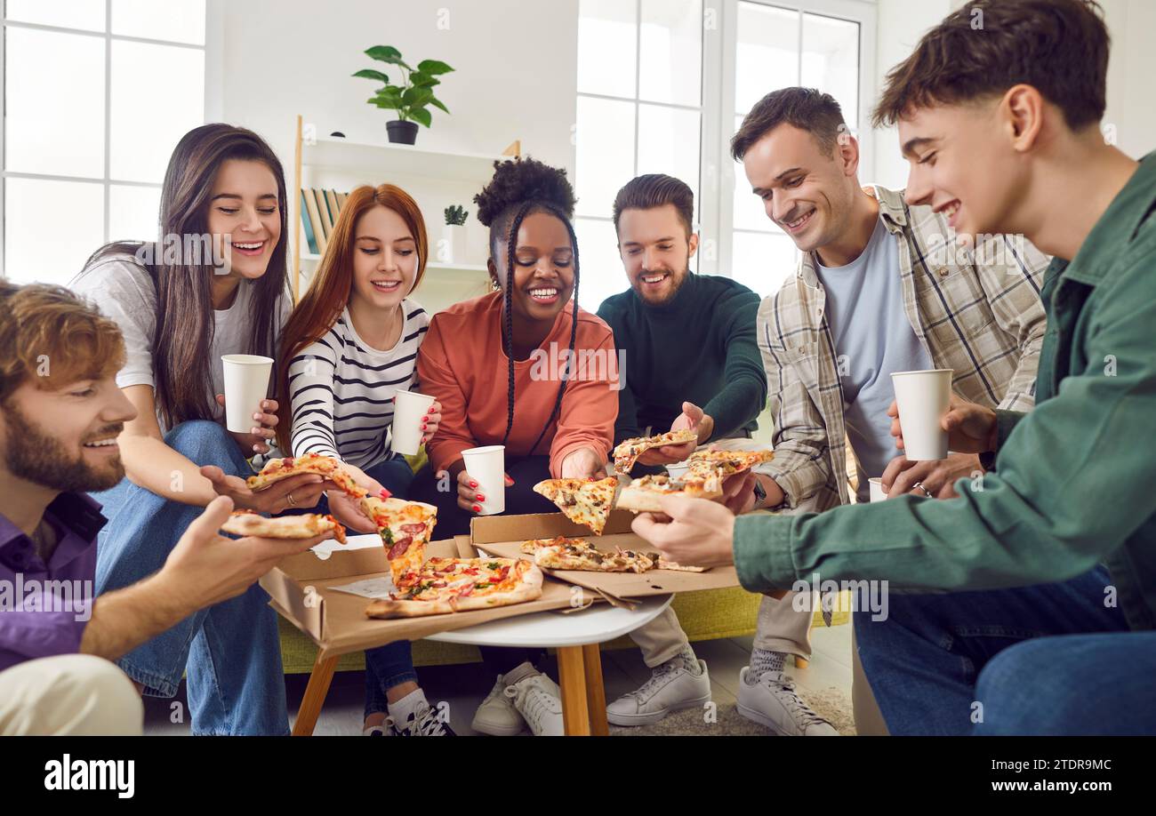 Amici felici e diversificati che si riuniscono a casa mangiando pizza parlando e ridendo insieme Foto Stock