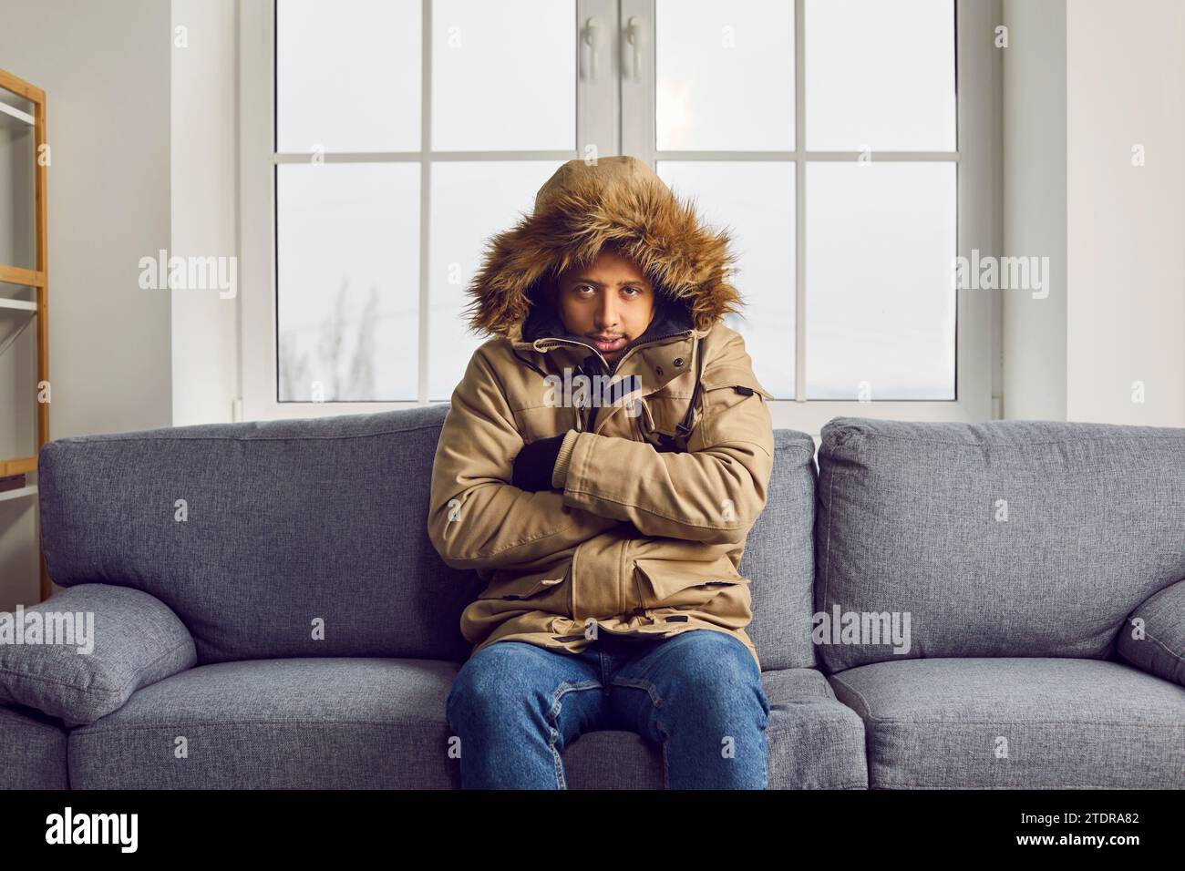 Un uomo gelido con una giacca calda seduto sul divano a casa Foto Stock
