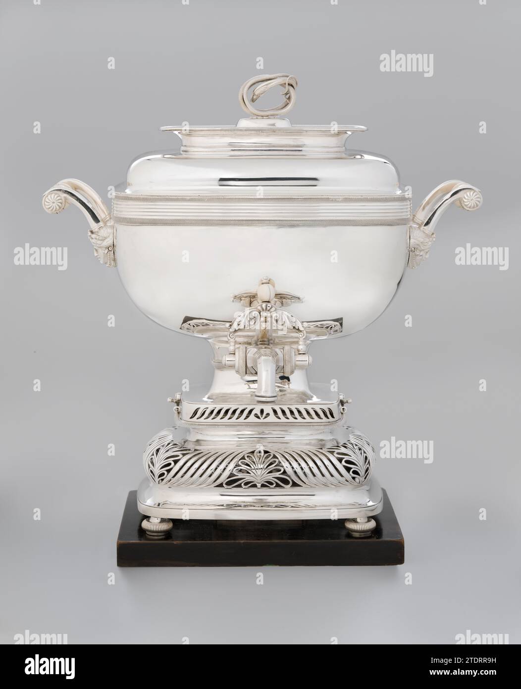 Tea Urn, azienda Bennewitz a zone, 1828 la ciotola rettangolare (B) con angoli arrotondati poggia su quattro zampe rotonde, convesse, con nervature verticali e a volte, ringiovanenti, attaccate alla base. È costituito da una base ad ala destra, una parte concava, una parte aperta a globo e una parte ristretta, sopra di essa un bordo convesso verticalmente scanalato, al quale sono fissati due occhi, e una parete diritta, rialzata, aperta. La parte aperta del Komfoor mostra curve a forma di S e al centro di ogni lato e sugli angoli dei palmeti. Il muro di coronamento è aperto sulla parte anteriore e posteriore con simili Foto Stock