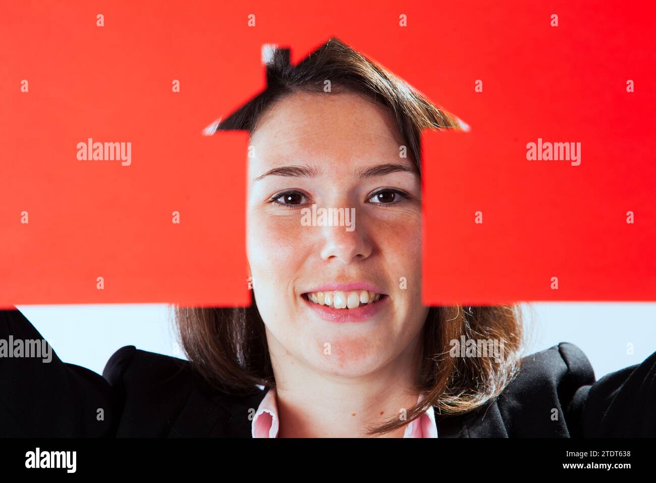 Una donna che si affaccia dietro una carta rossa tagliata a forma di casa Foto Stock