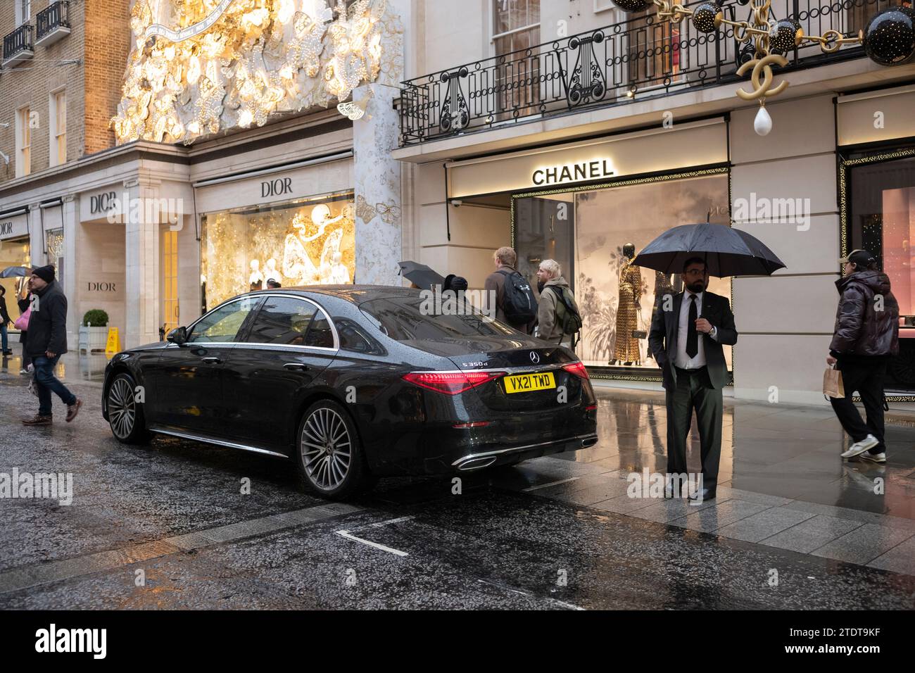 Un autista attende che la sua clientela ritorni dallo shopping di beni di lusso di Natale lungo Old Bond Street in una giornata invernale umida, Londra, Inghilterra Foto Stock