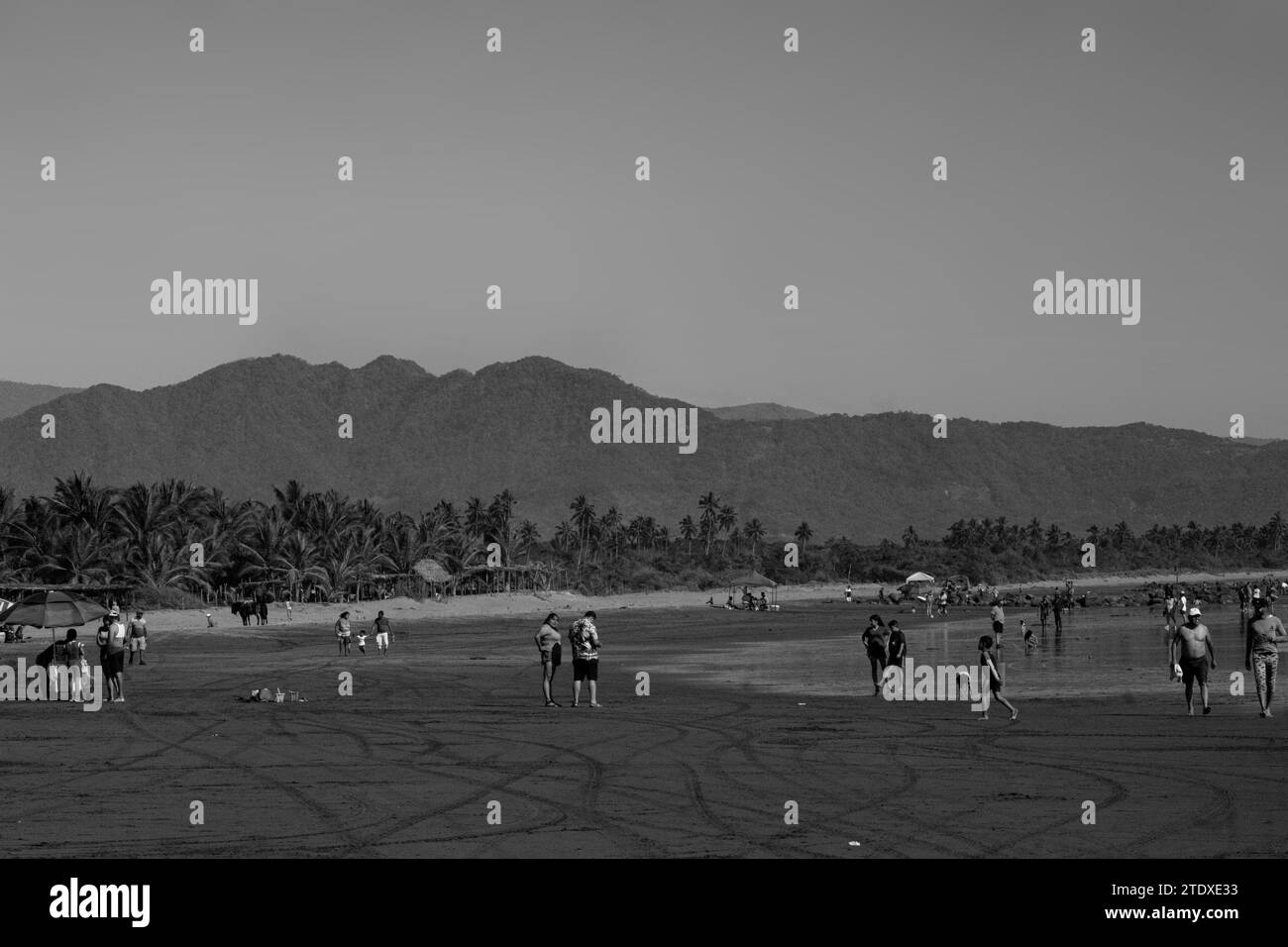 Un'affascinante miscela di sole, sabbia e mare, dove gli amanti della spiaggia incontrano l'orizzonte, incorniciati da montagne lontane nell'abbraccio di una fuga costiera. Foto Stock