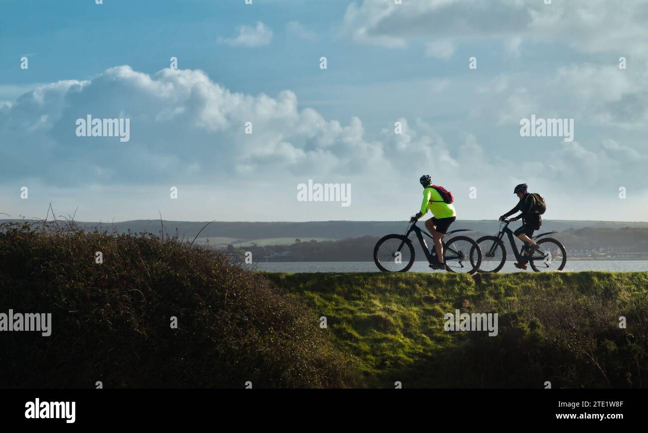 Due, Una coppia di , ciclisti in bicicletta sul muro del Mare di Keyhaven con l'Isola DI Wight e il Solent sullo sfondo, Regno Unito Foto Stock