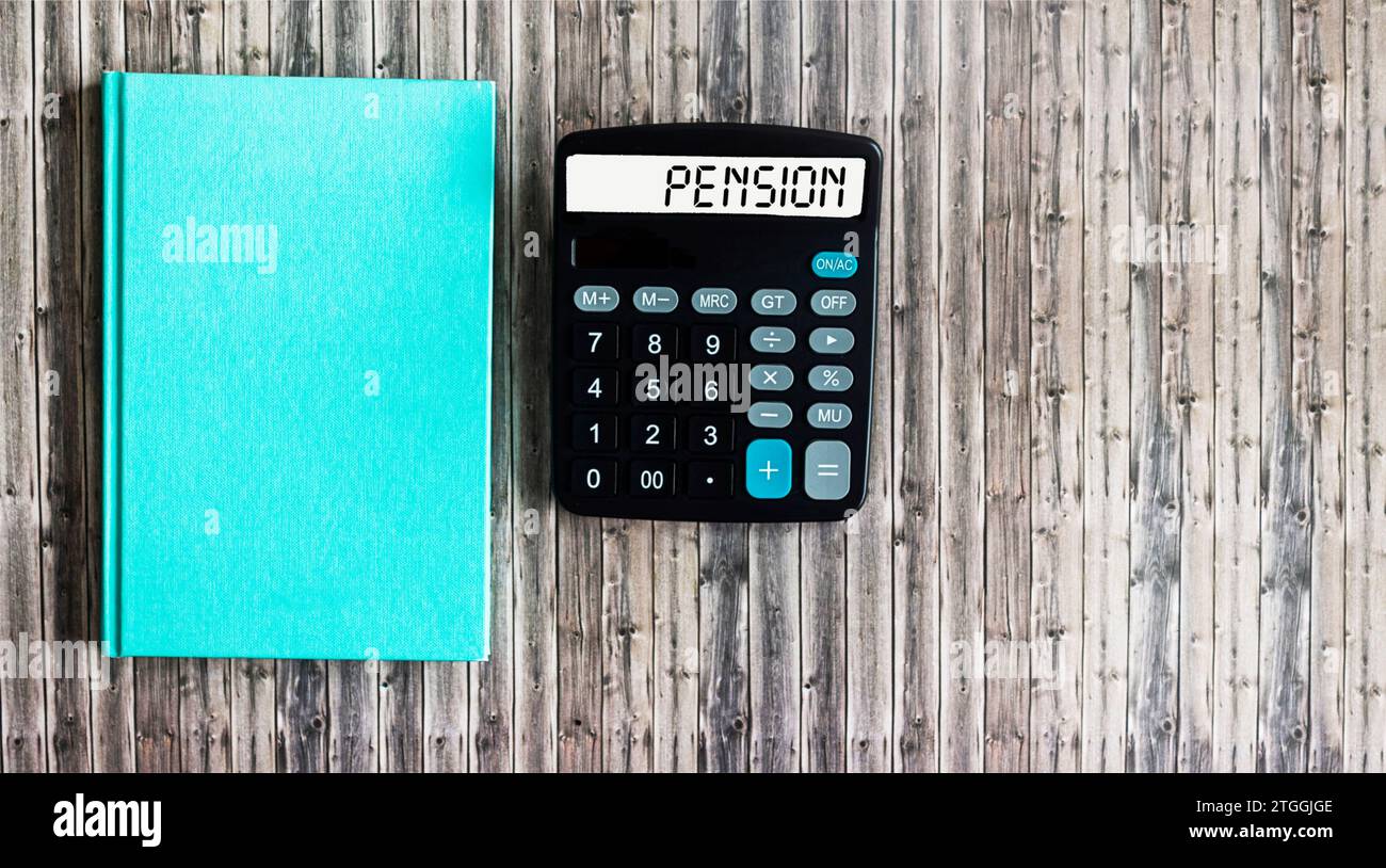 Su uno sfondo di legno, una calcolatrice con l'iscrizione PENSIONE sulla lavagna, un blocco note verde. Concetto aziendale Foto Stock
