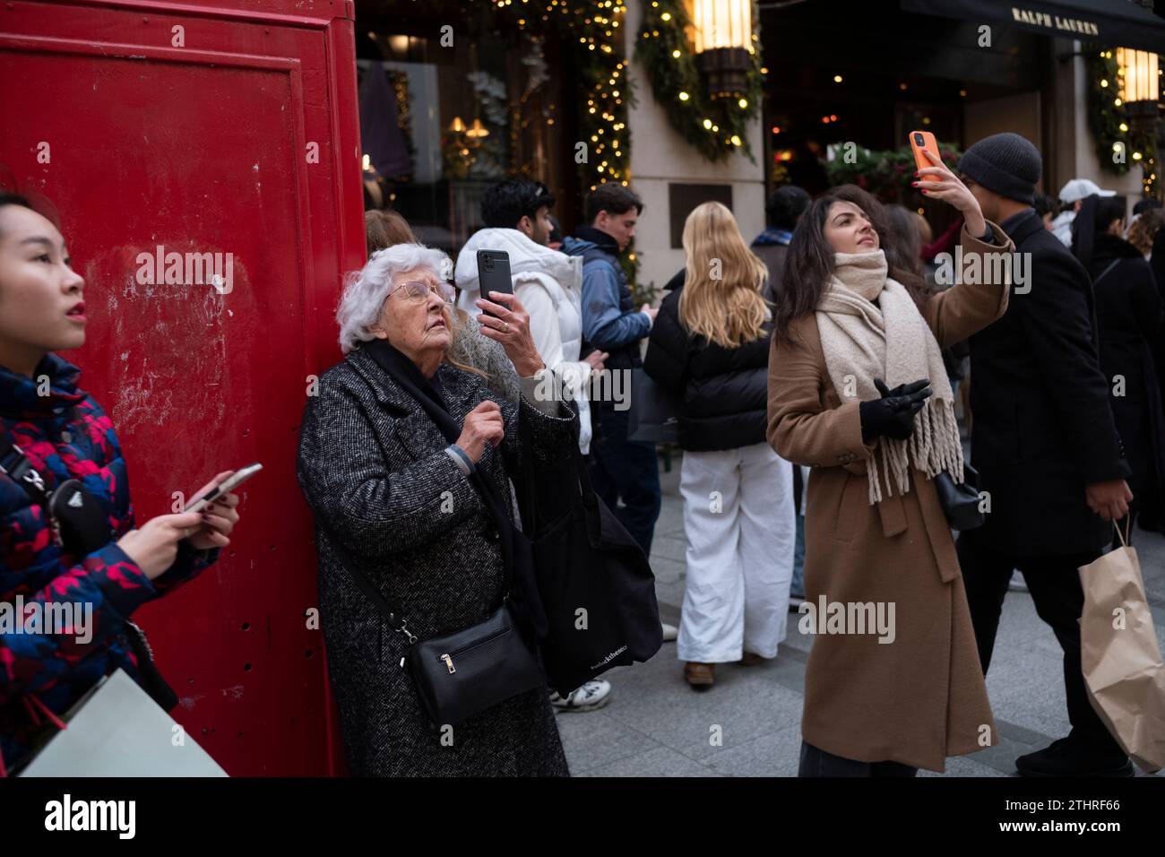 I turisti festivi in giro per la città scattano selfie e foto delle esposizioni di Natale lungo Old Bond Street, nel cuore della Mayfair di Londra, 20 dicembre 2023. Foto Stock