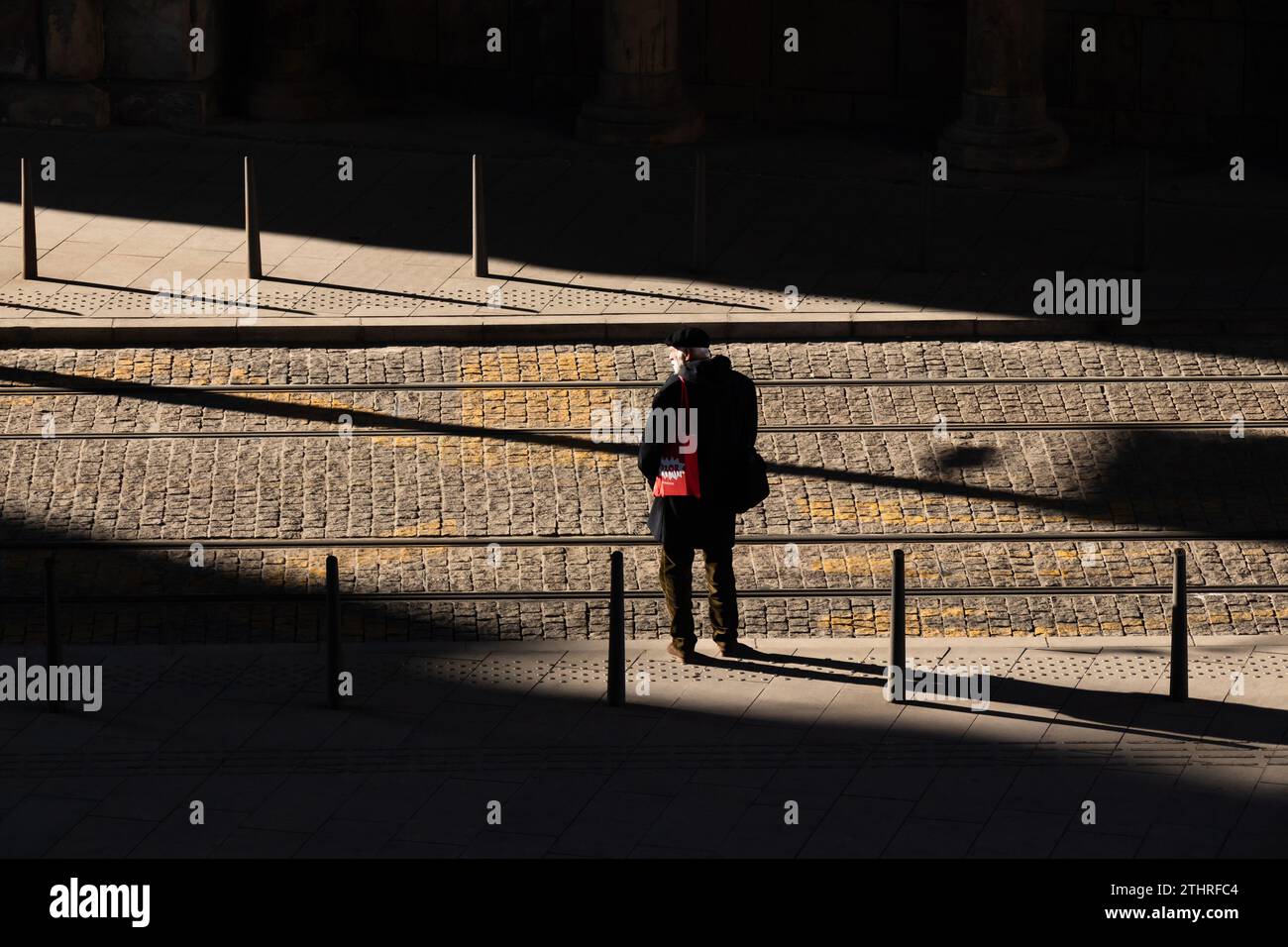 Beograd, Serbia - 19 dicembre 2023: Un uomo con la barba bianca in piedi da solo su un marciapiede pavimentato con rotaie del tram, alla luce del sole, il giorno d'inverno con S Foto Stock