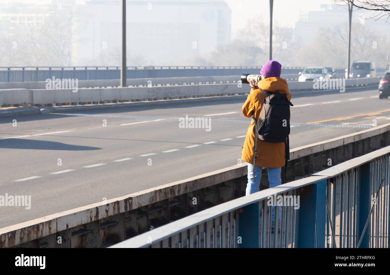 Una fotografa di strada in piedi sul ponte e fotografa con la macchina fotografica, in una giornata inquinata in nebbia, da dietro Foto Stock