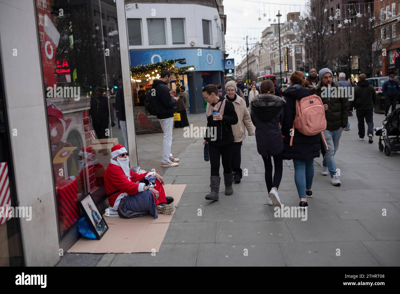 Un senzatetto vestito da Babbo Natale siede su un cartone mentre cerca di ottenere donazioni lungo Oxford Street per una notte a Londra, Regno Unito Foto Stock