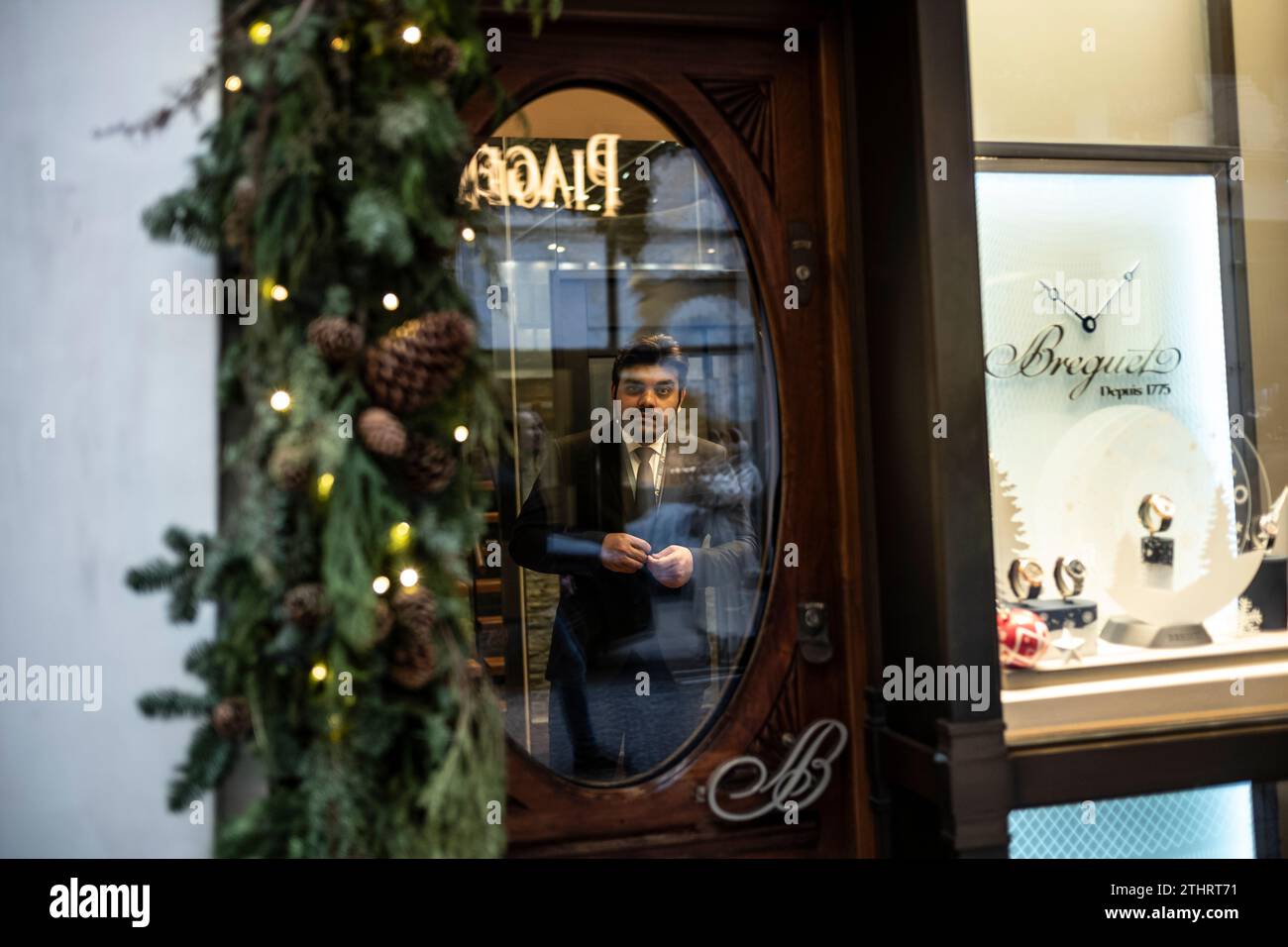 Un lavoratore di gioielleria si affaccia sulla finestra circolare della porta su Old Bond Street nel cuore della Mayfair di Londra, 20 dicembre 2023. Foto Stock