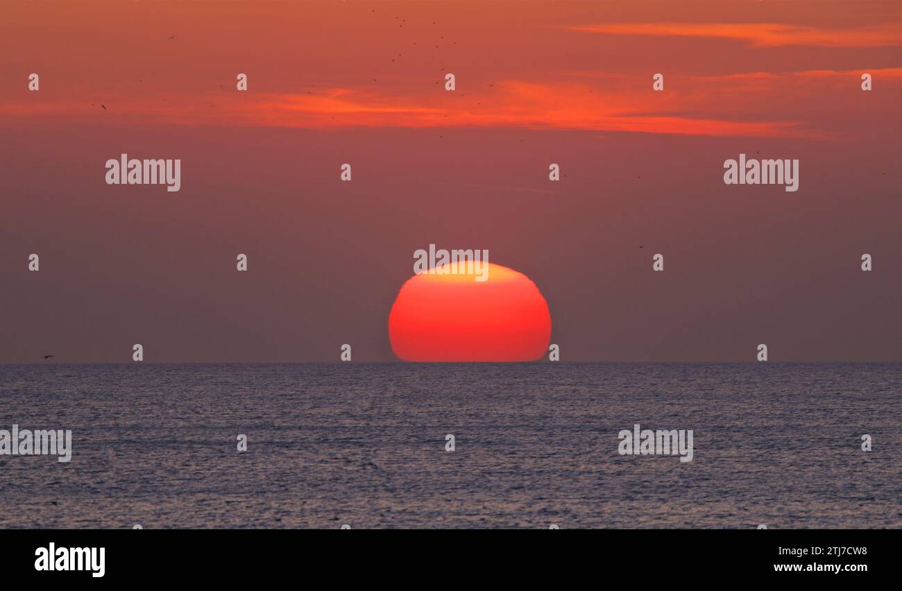 Il sole che tramonta. Un disco rosso/arancione nel cielo. Foto Stock