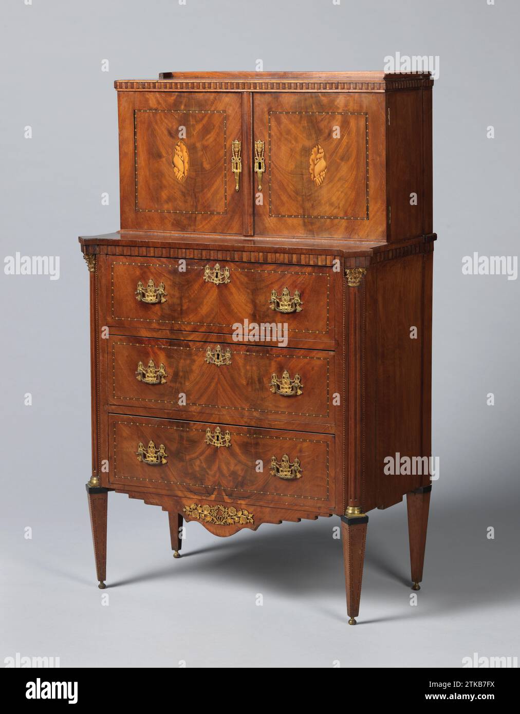 Armadio con due ante e tre cassetti, incollato con mogano. Sulle ante un motivo centrale a conchiglia ovale, Anonymous, 1780 armadio in quercia con credenza superiore, incollato con mogano. Le zampe coniche e gli stili angolari, con mezzalune scanalate con basamento in rame e capitale corinzio, sono collocati sopra i porri. I tre cassetti della base trasportano impasto di rame dorato sotto forma di vasi con ghirlande sospese. Questi cassetti e i due sportelli dell'armadietto superiore presentano campi rettangolari e quadrati contrassegnati da pneumatici con motivo a spina di pesce; Un motivo a conchiglia ovale centrale sulle porte. Smerlato Foto Stock