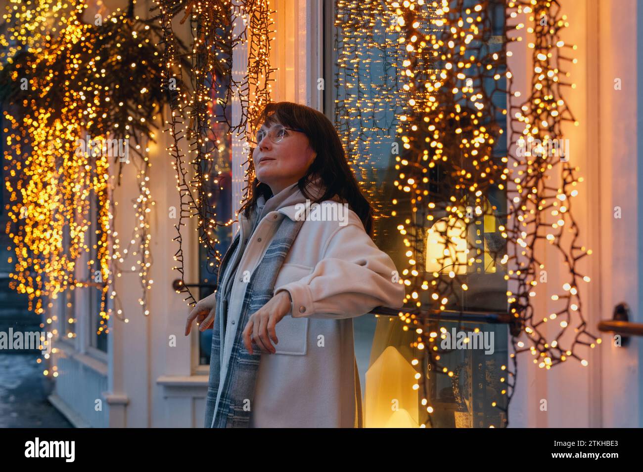 Una donna sorridente nel suo fiore all'occhiello, che respira il fascino di una città nordica decorata per Natale e Capodanno. Foto di alta qualità Foto Stock