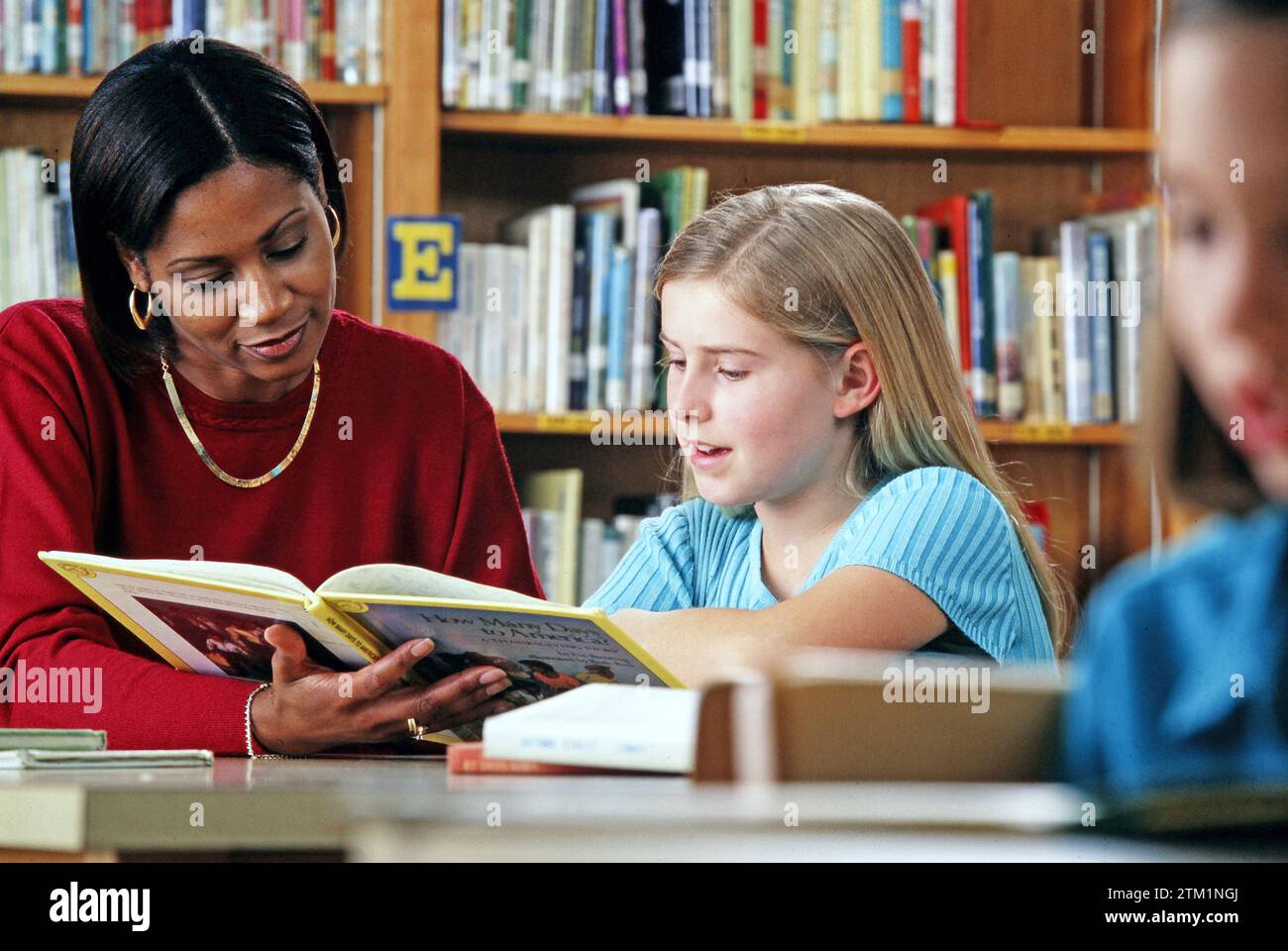 Un bibliotecario afro-americano che aiuta uno studente della scuola media caucasica a leggere un libro di scienze Foto Stock