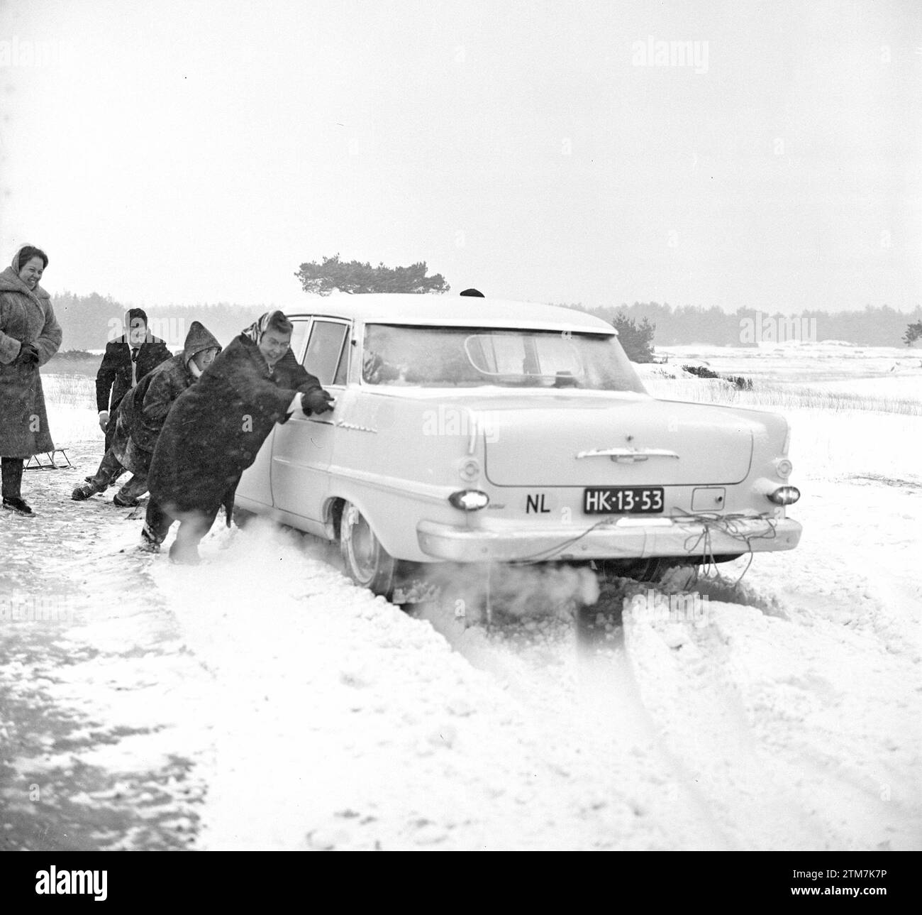 Uomini che spingono un'auto innevata su un'autostrada nei Paesi Bassi ca. 1° gennaio 1963 Foto Stock