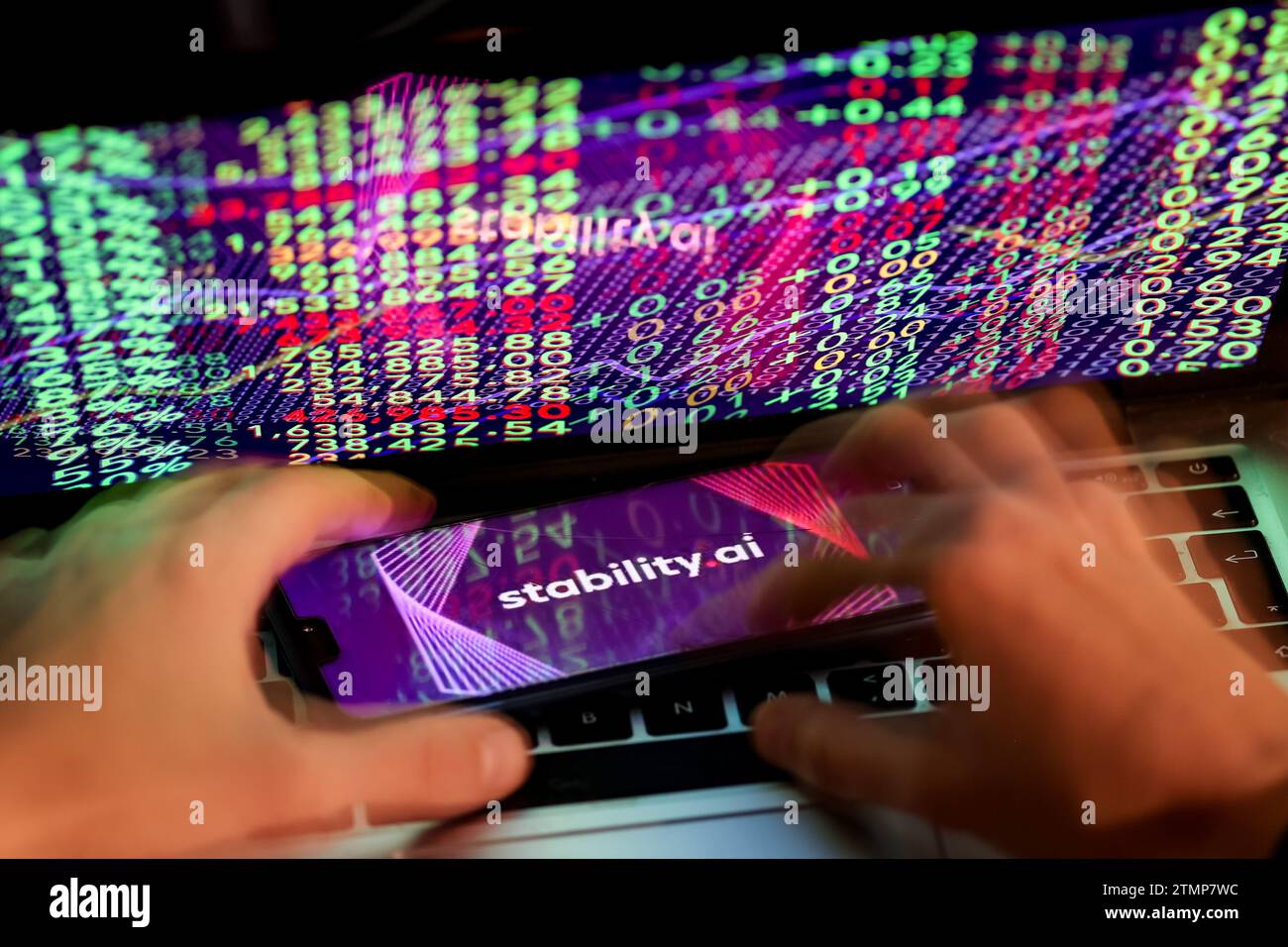 Cracovia, Polonia, 20 dicembre 2023. Questa foto mostra un logo dell'app Stability.ai visualizzata su uno smartphone e mani umane che lavorano su un computer con i numeri di mercato azionario sullo sfondo. Foto Stock