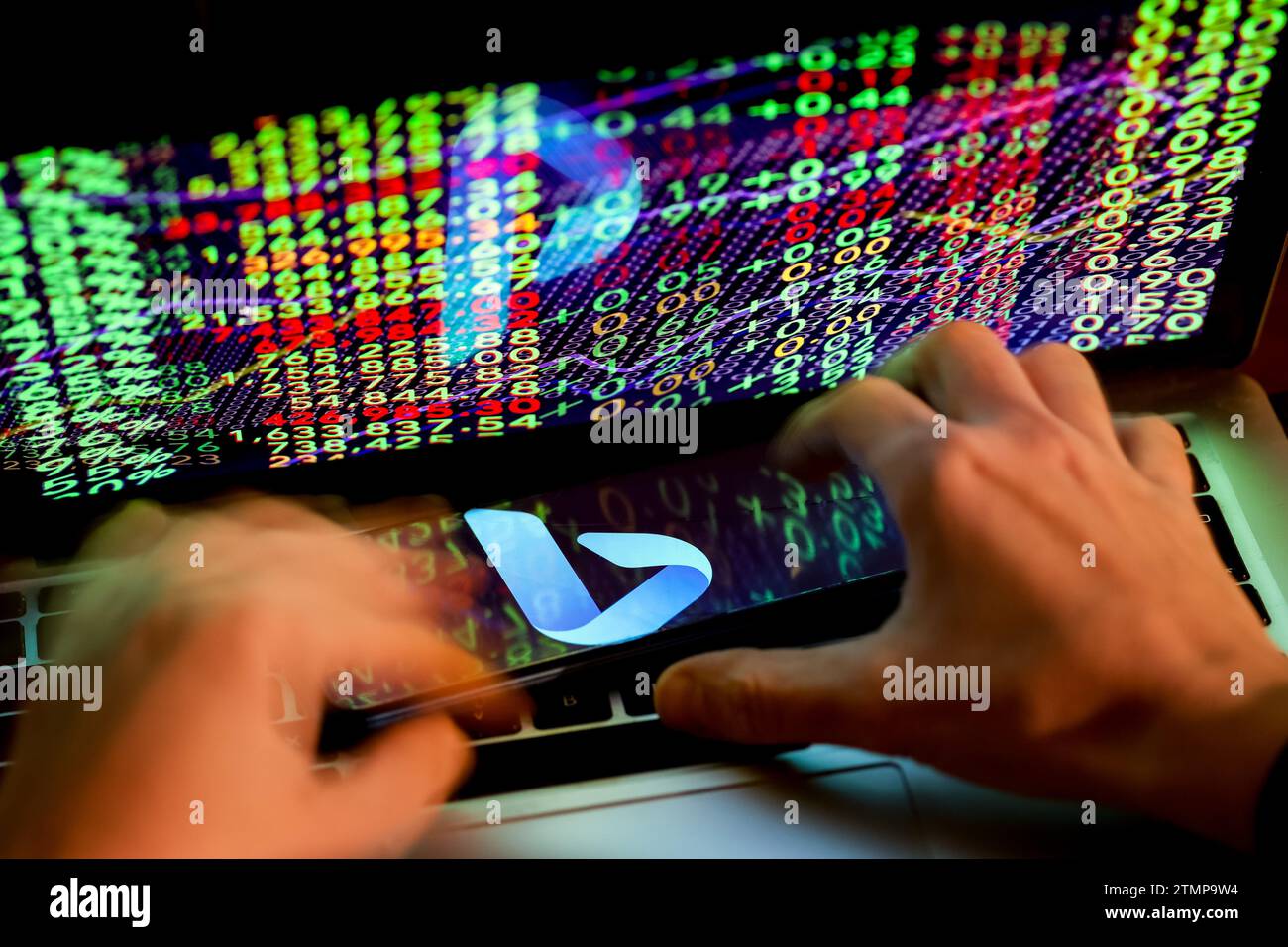 Cracovia, Polonia, 20 dicembre 2023. Questa fotografia illustra un logo dell'app Bing ai visualizzata su uno smartphone e mani umane che lavorano su un computer con i numeri del mercato azionario sullo sfondo. Foto Stock