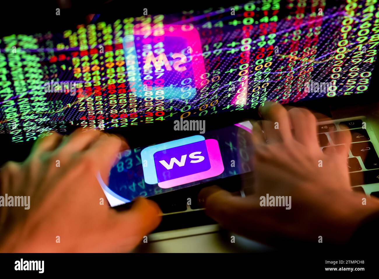 Cracovia, Polonia, 20 dicembre 2023. Questa fotografia illustra un logo dell'app Writesonic ai visualizzato su uno smartphone e mani umane che lavorano su un computer con i numeri di borsa sullo sfondo. Foto Stock