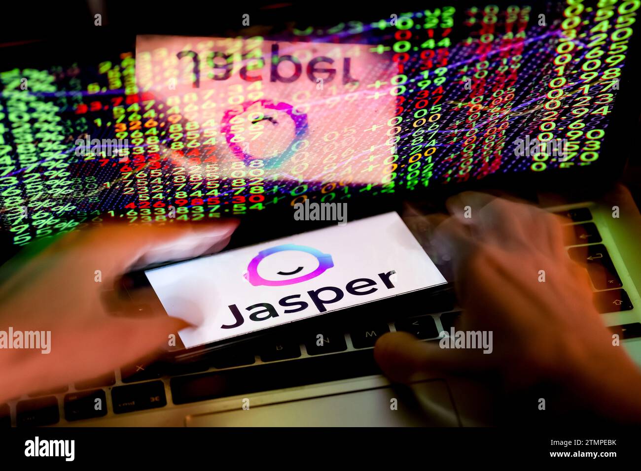 Cracovia, Polonia, 20 dicembre 2023. Questa foto mostra un logo dell'app Jasper ai visualizzato su uno smartphone e mani umane che lavorano su un computer con i numeri di borsa sullo sfondo. Foto Stock