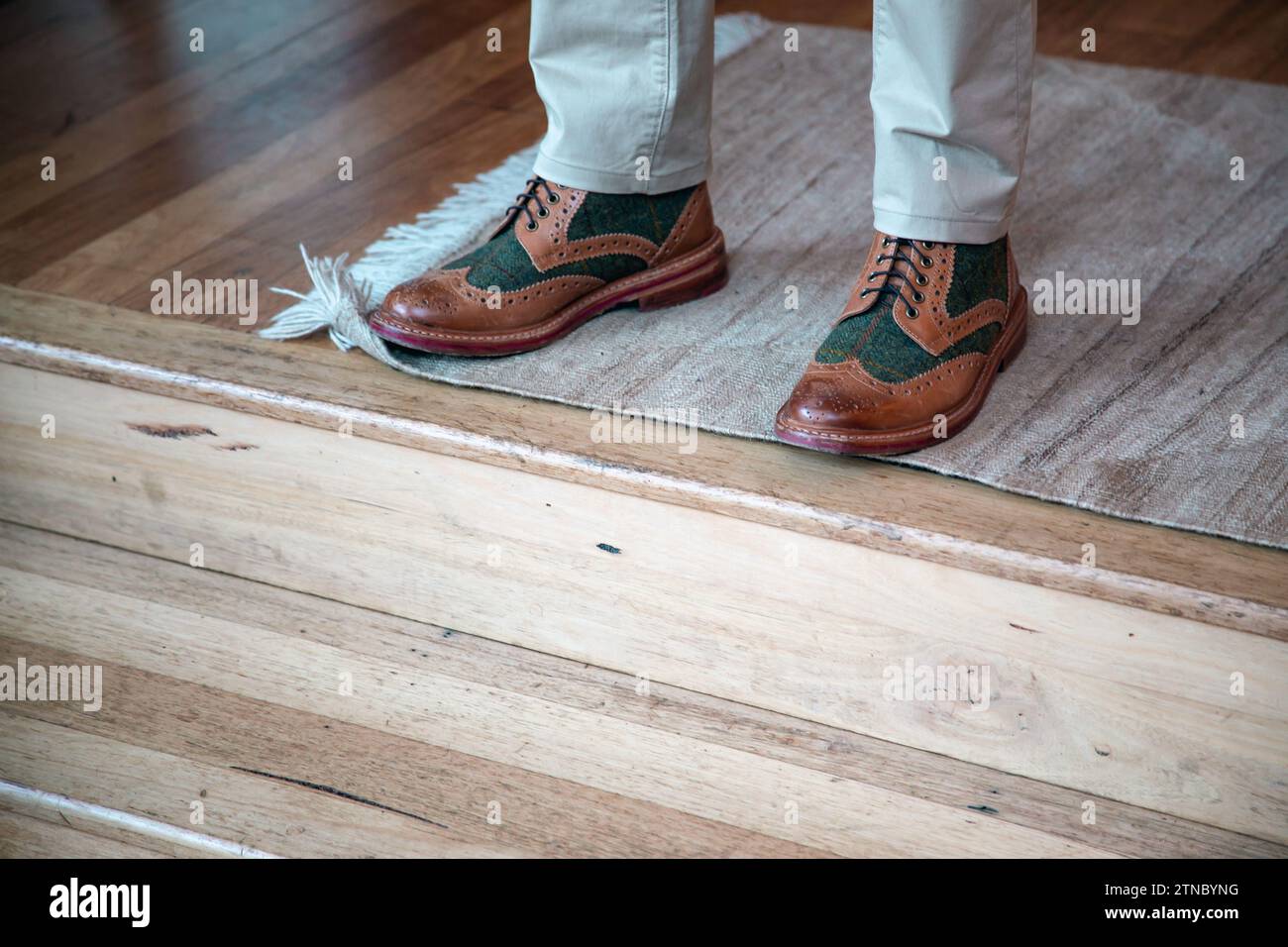 Un uomo ben vestito che indossa scarpe di pelle il giorno del suo matrimonio si erge sul tappeto di lana intrecciata sopra le scale di legno mentre attende l'inizio della cerimonia Foto Stock