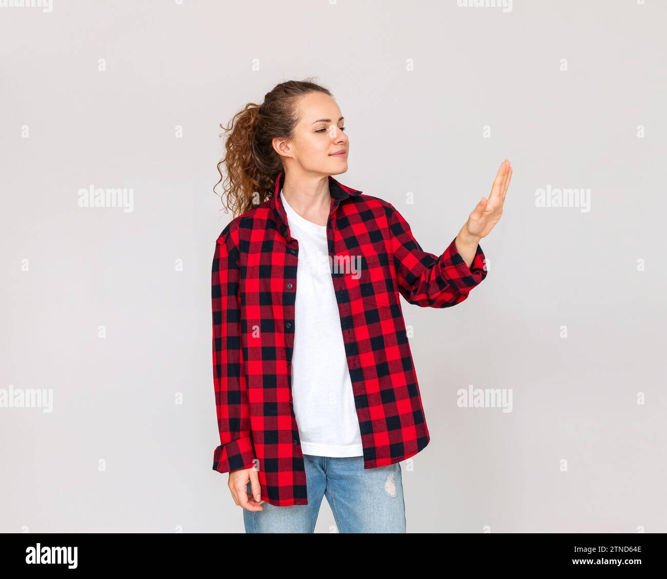 Donna con un abito casual che guarda una nuova manicure sulla mano e sorride davanti a uno sfondo semplice in studio. Foto Stock