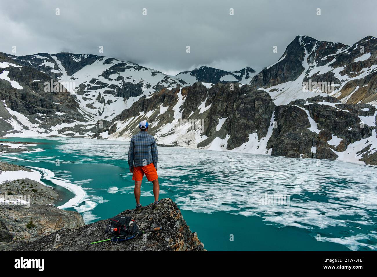 L'escursionista solitario osserva la distesa ghiacciata del lago Wedgemount, abbracciando la solitudine. Foto Stock