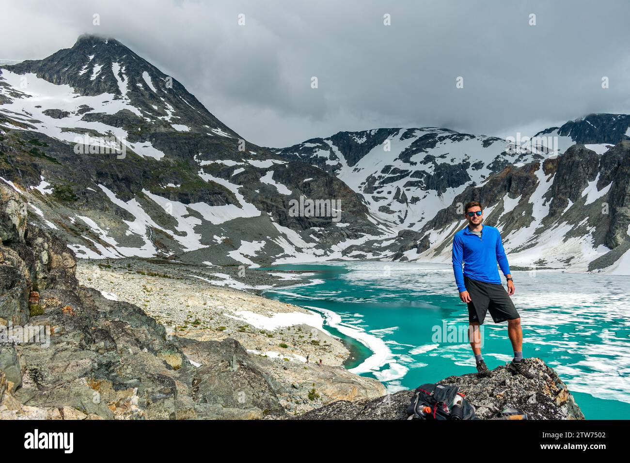 Un avventuriero in posa si trova vicino al vivace lago Wedgemount, pronto per la salita. Foto Stock