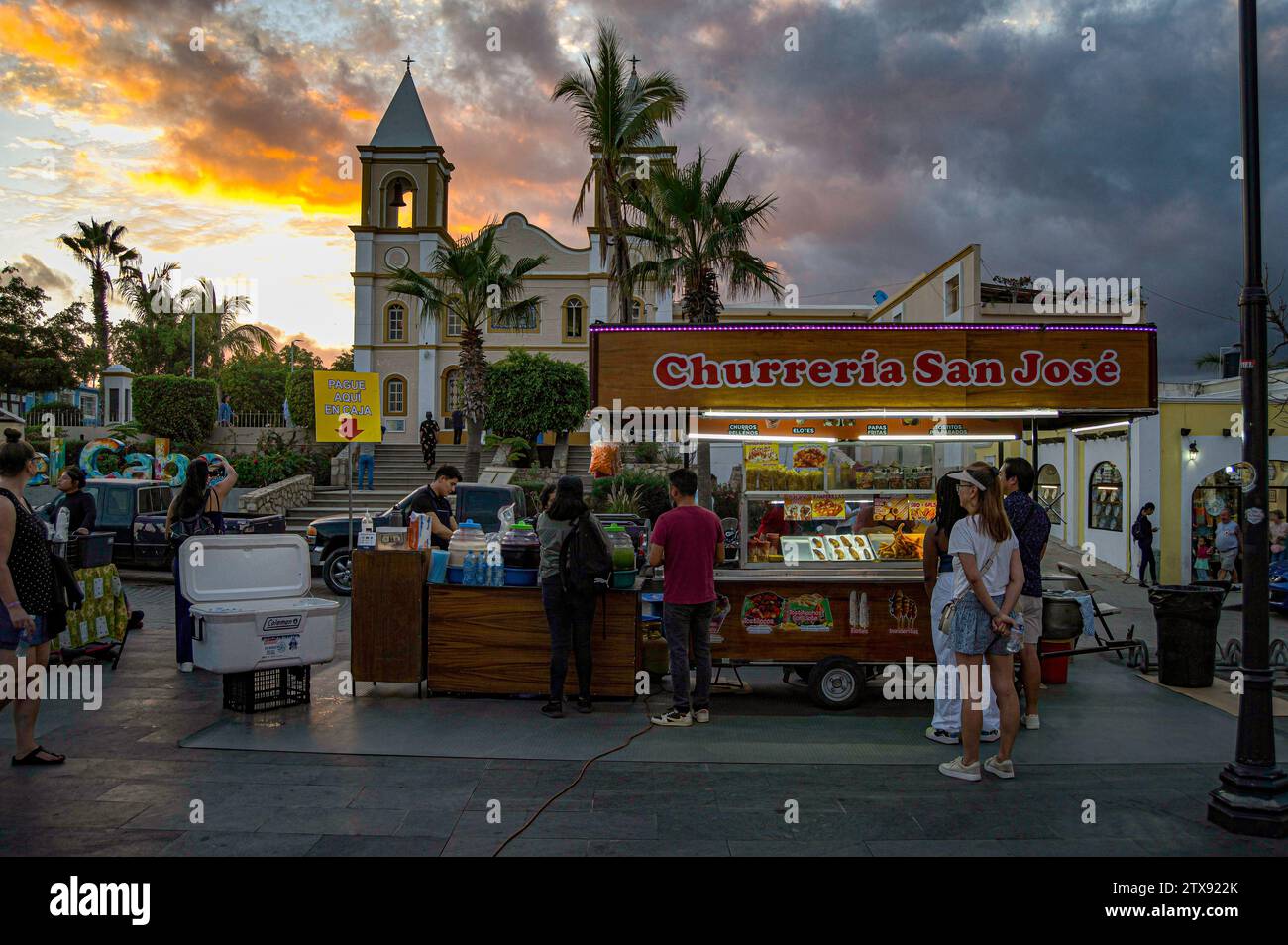 Foto serale della Churreria San Jose che vende churros (una pasticceria messicana) durante l'artwalk settimanale con la missione della città sullo sfondo. Foto Stock