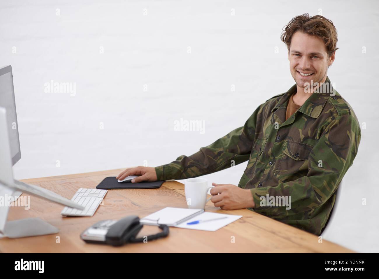 Militare in carica, ricerca alla scrivania e sorridi in ritratto con le operazioni militari e raccogli informazioni online. Giovane soldato con tazza di caffè Foto Stock