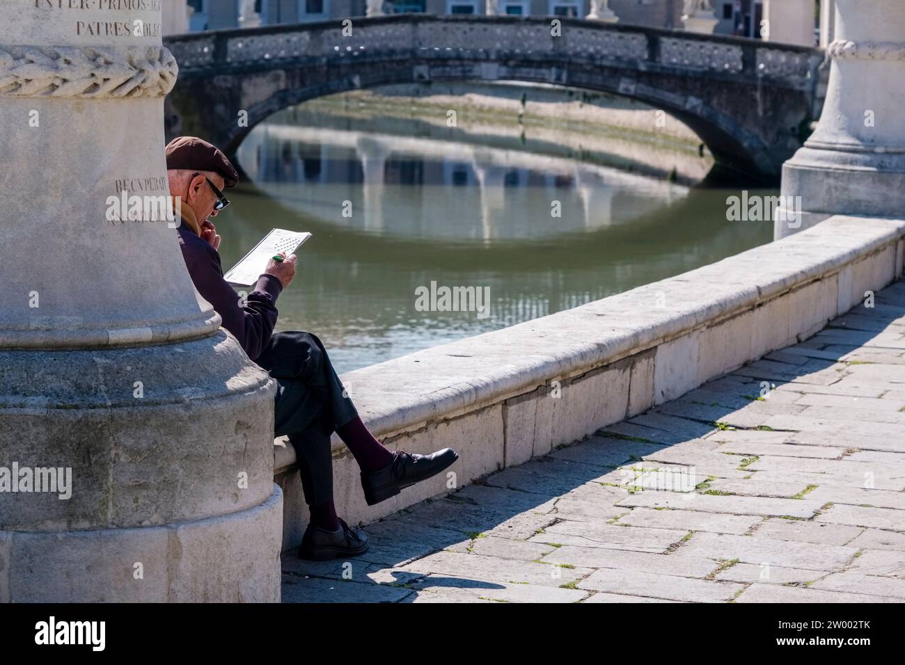 Un vecchio seduto a leggere ai piedi di una statua sull'Isola Memmia. Foto Stock