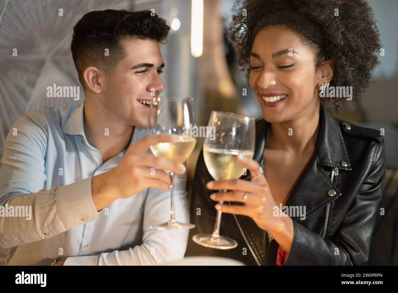 Una giovane coppia brindisce con un bicchiere di vino bianco, godendosi un momento intimo insieme in un accogliente ambiente del ristorante. Foto Stock