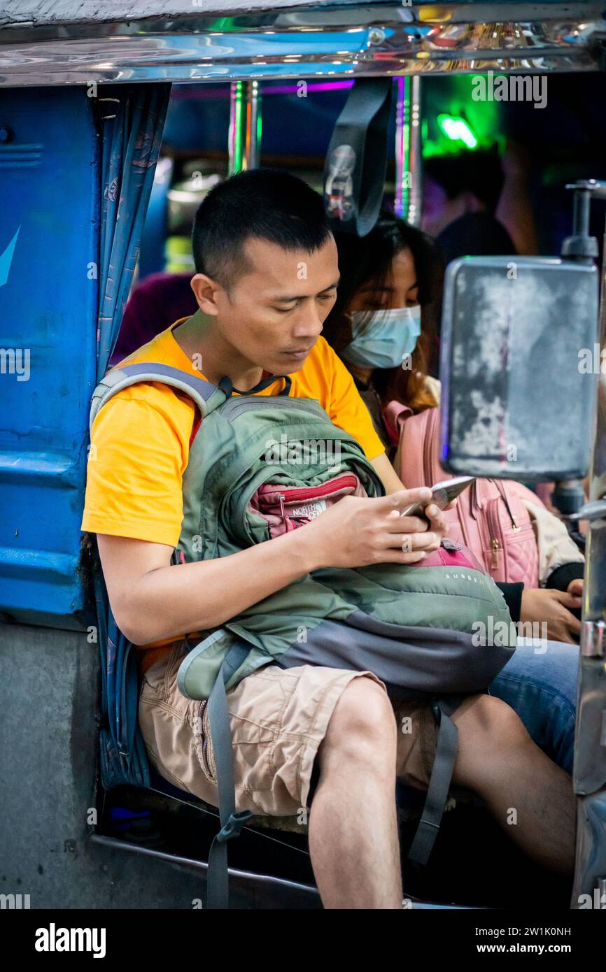 Un uomo filippino fa scorrere uno dei suoi cellulari seduto su un jeepney di Manila. Foto Stock