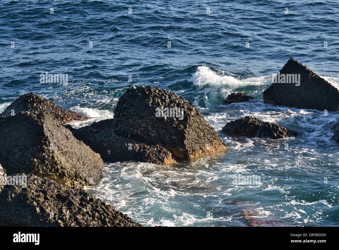 Serenità costiera: Rocce marine che resistono al dolce abbraccio di piccole onde lungo la riva. Foto Stock