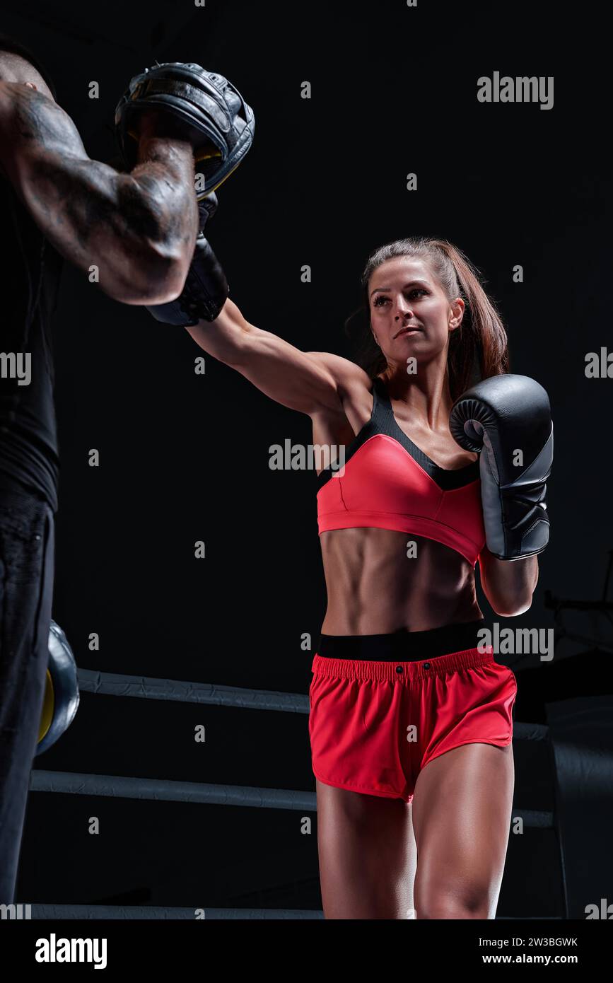 Donna atletica in pantaloncini rossi e top pugilato con un allenatore. Boxe e arti marziali miste. Supporti misti Foto Stock