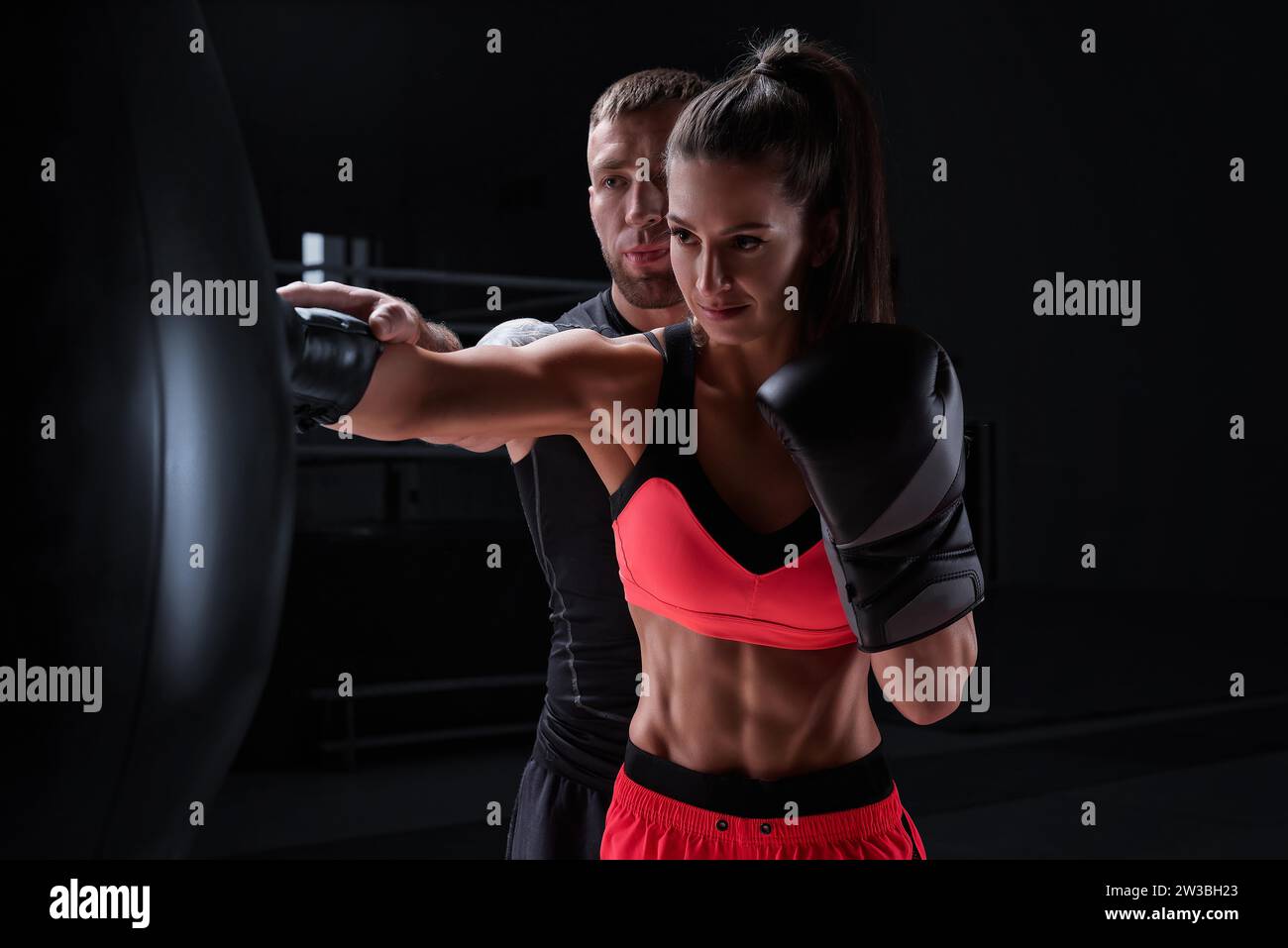 Donna atletica in pantaloncini rossi e top pugilato con un allenatore. Boxe e arti marziali miste. Supporti misti Foto Stock